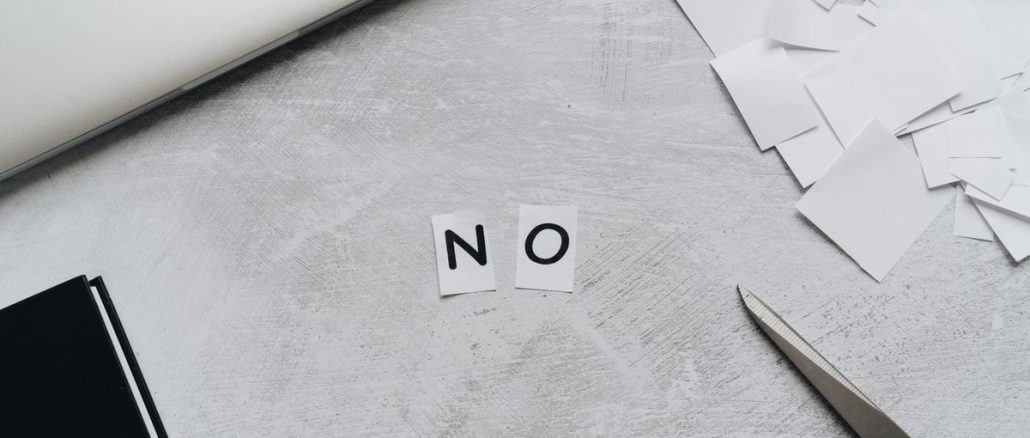 Aus Papierschnipseln gelegtes Wort „NO“ neben Laptop und Schere auf hellem Untergrund