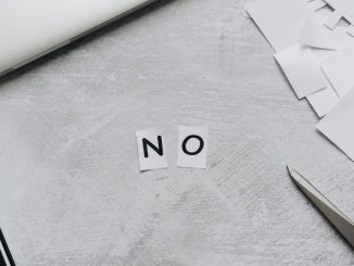 Aus Papierschnipseln gelegtes Wort „NO“ neben Laptop und Schere auf hellem Untergrund