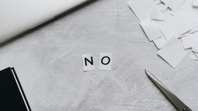 Aus Papierschnipseln gelegtes Wort „NO“ neben Laptop und Schere auf hellem Untergrund