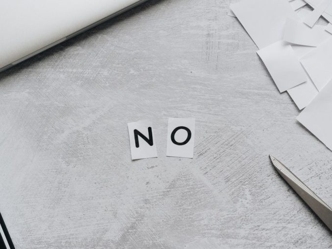 Aus Papierschnipseln gelegtes Wort „NO“ neben Laptop und Schere auf hellem Untergrund